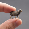 Fingertip-sized miniature brass sheep figurine held between fingers, showing true scale